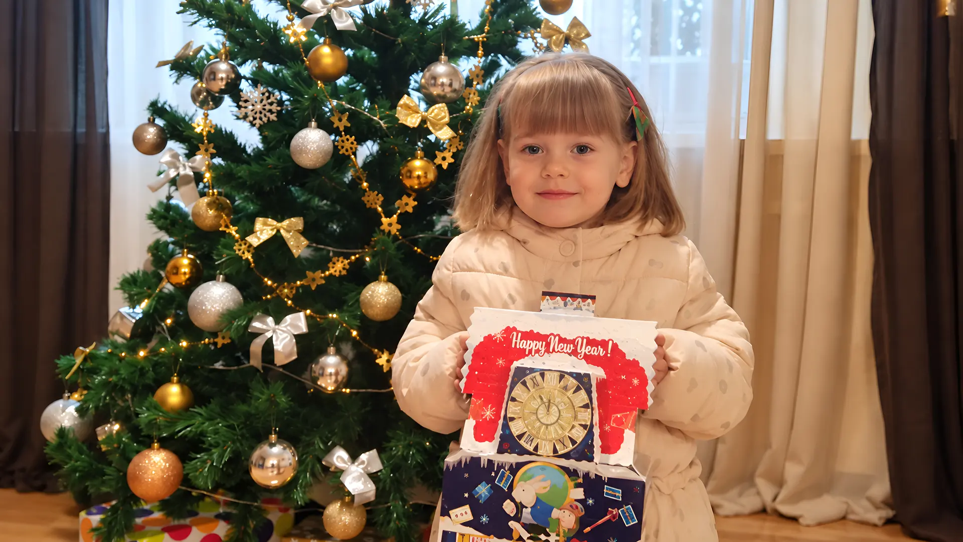 A girl stands at home by a Christmas tree holding a gift from the Grow Up in a Family foundation team