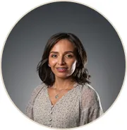Smiling woman with shoulder-length dark hair wearing a light gray blouse against a gray background.