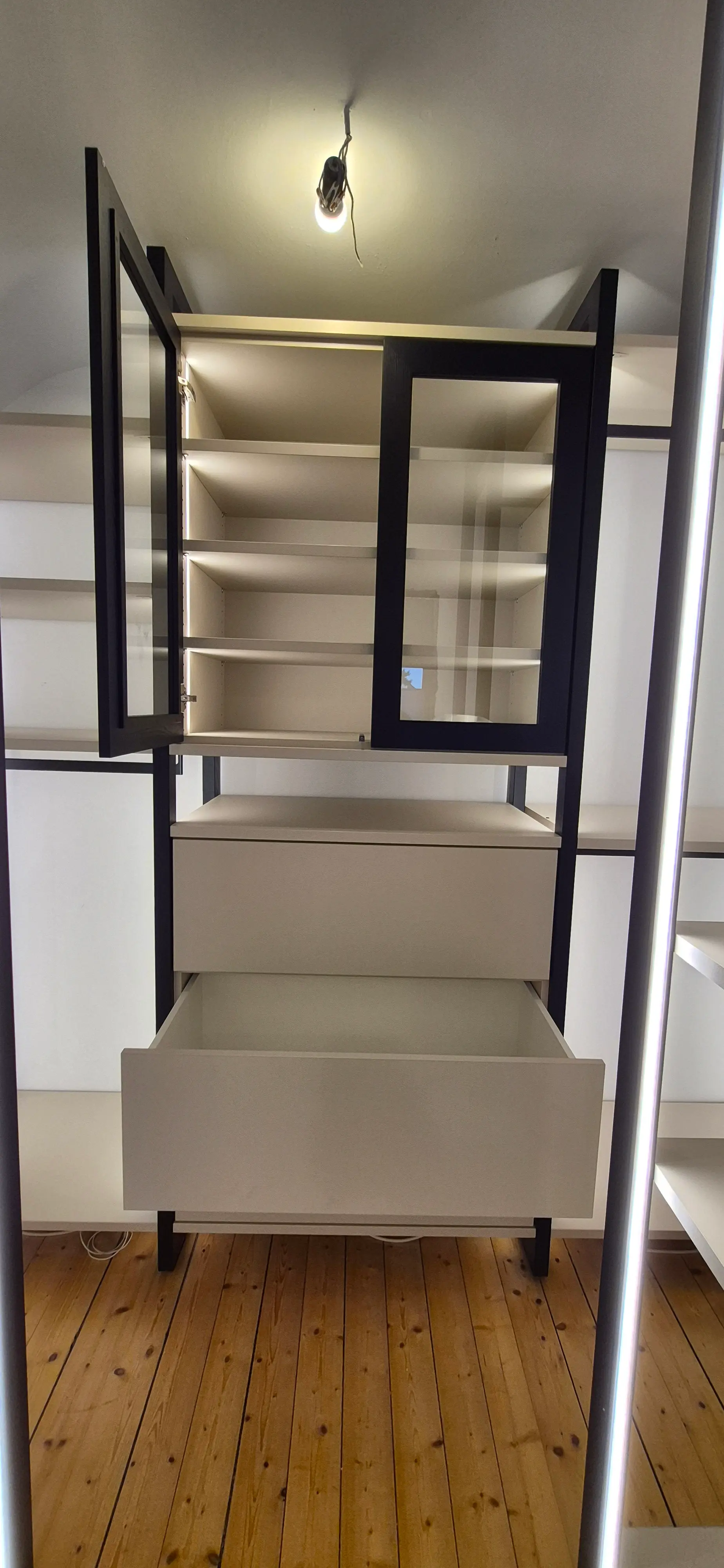 Maßgefertigtes Ankleidezimmer in Viernheim mit geöffneter Schublade, Glasvitrine und beleuchtetem Regalsystem
