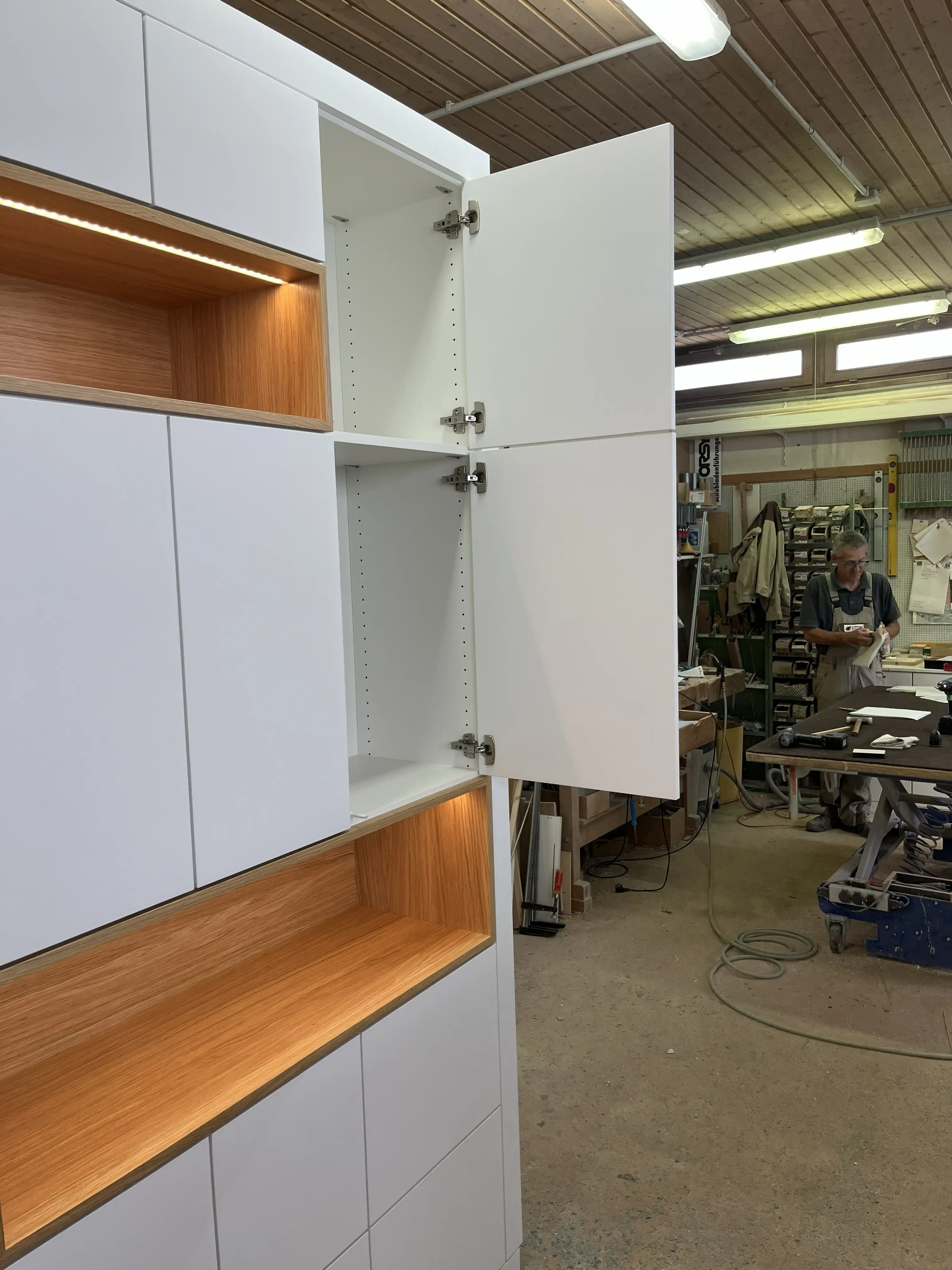 Geöffnete Tür eines maßgefertigten Wohnraummöbels mit weißen Fronten und beleuchteten Eiche-Nischen in Viernheim.