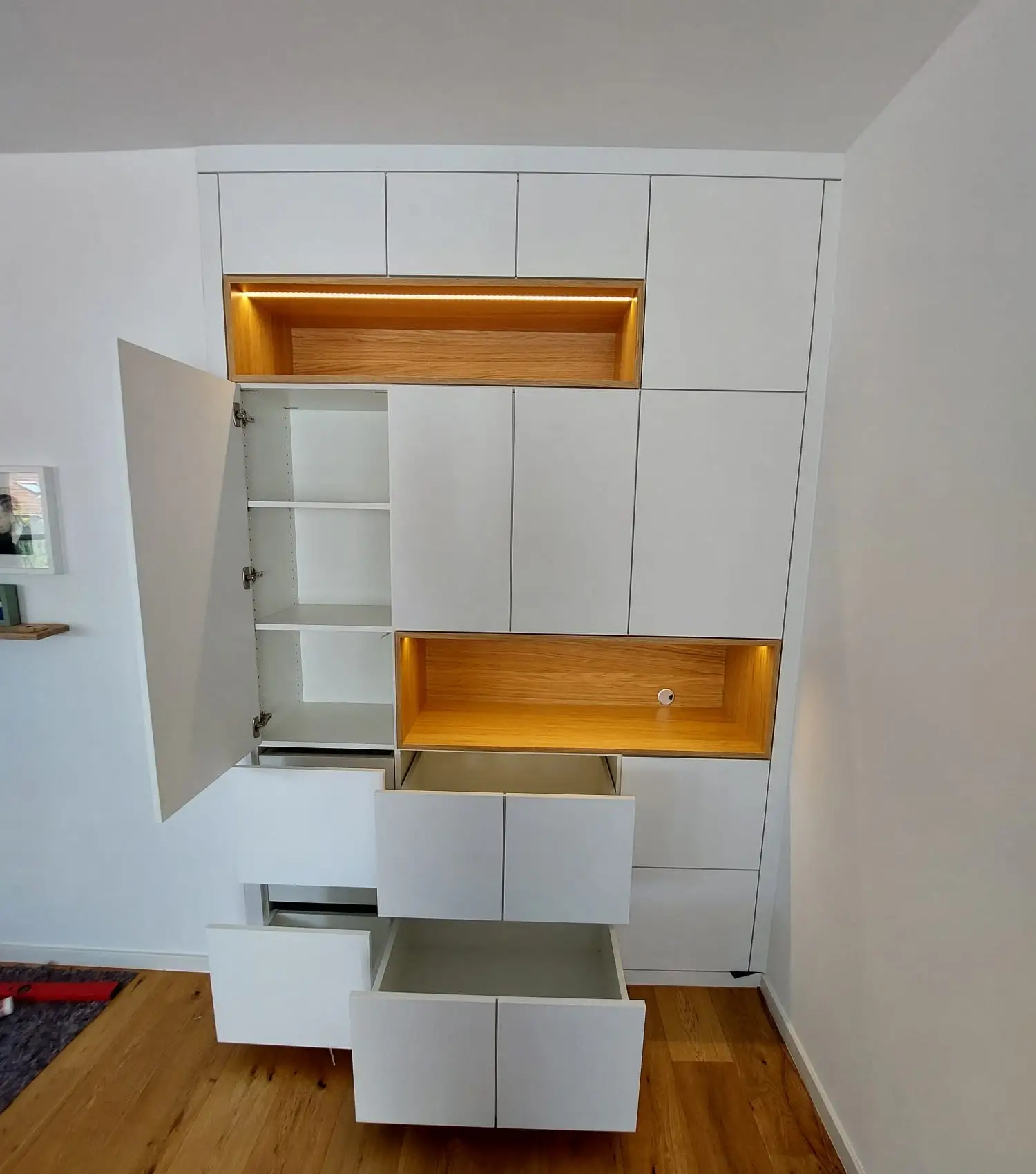 Maßgefertigtes Wohnraummöbel mit geöffneten Schubkästen, Hochschrank und beleuchteten Eiche-Nischen in Viernheim.