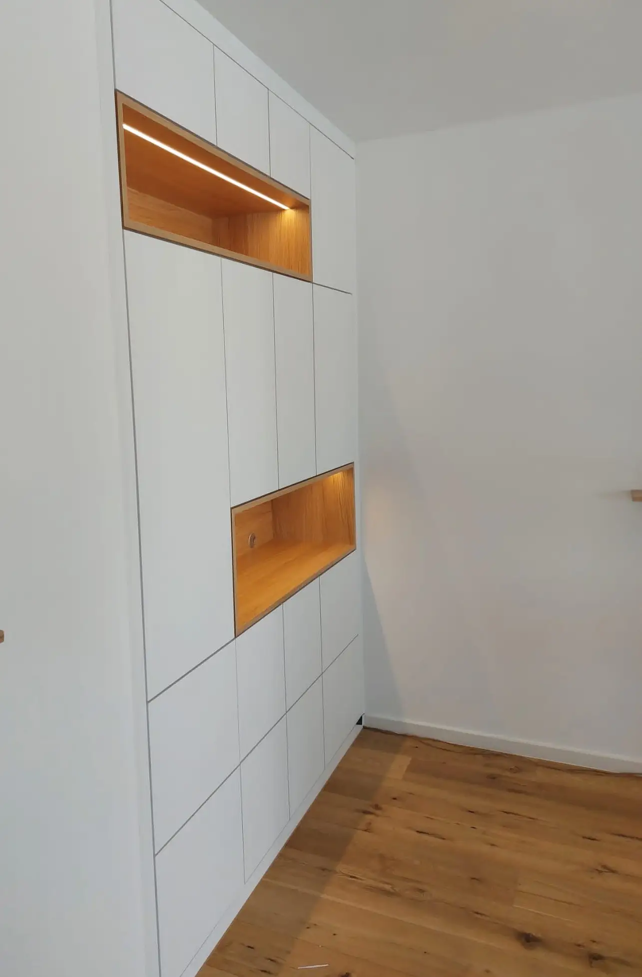 Seitenansicht eines maßgefertigten Wohnraummöbels mit weißen Fronten und beleuchteten Eiche-Nischen in Viernheim