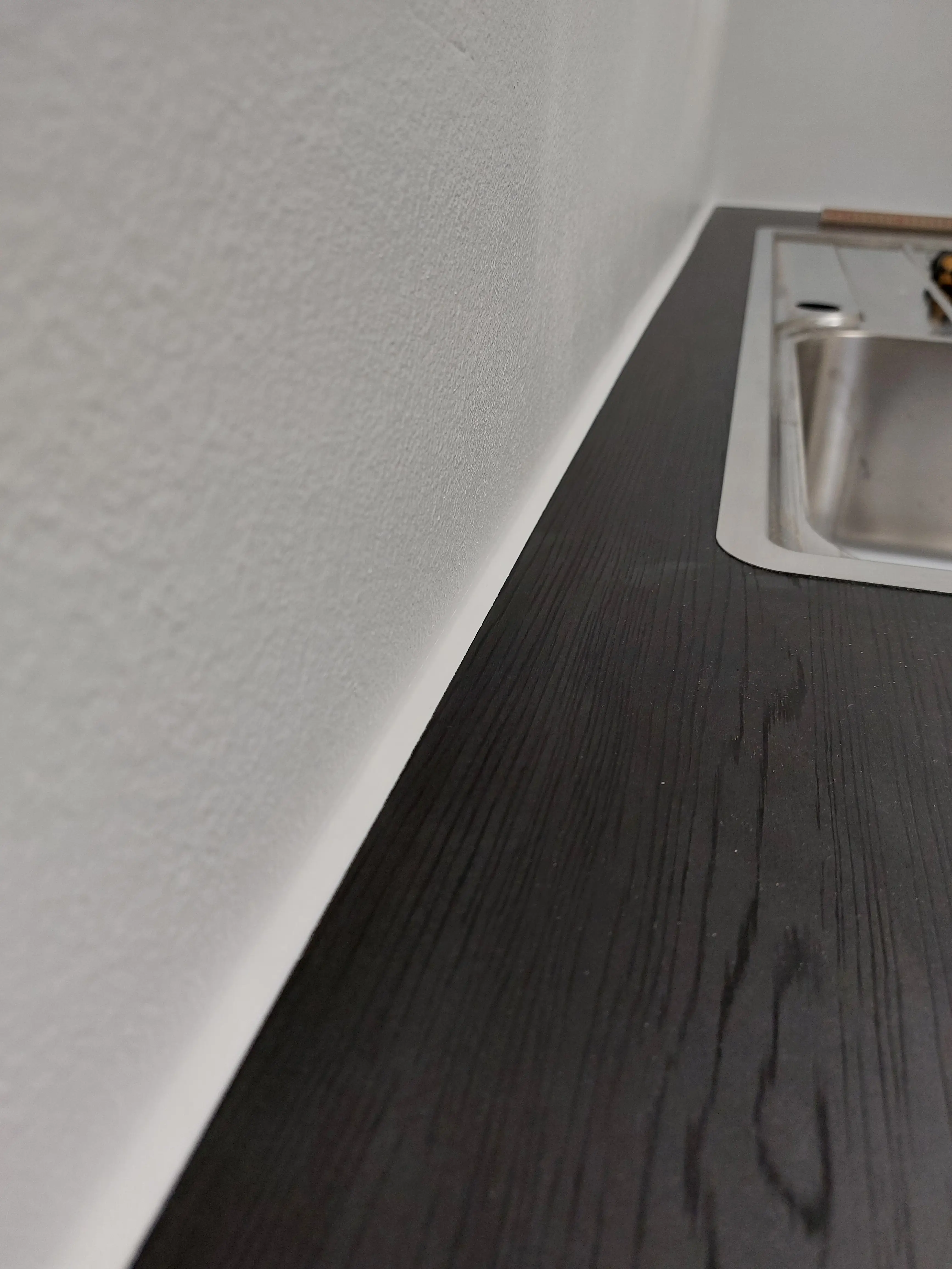 Detailaufnahme der schwarzen HPL-Arbeitsplatte in Esche-Optik mit sauberem Wandanschluss im maßgefertigten Hauswirtschaftsraum in Walldorf.