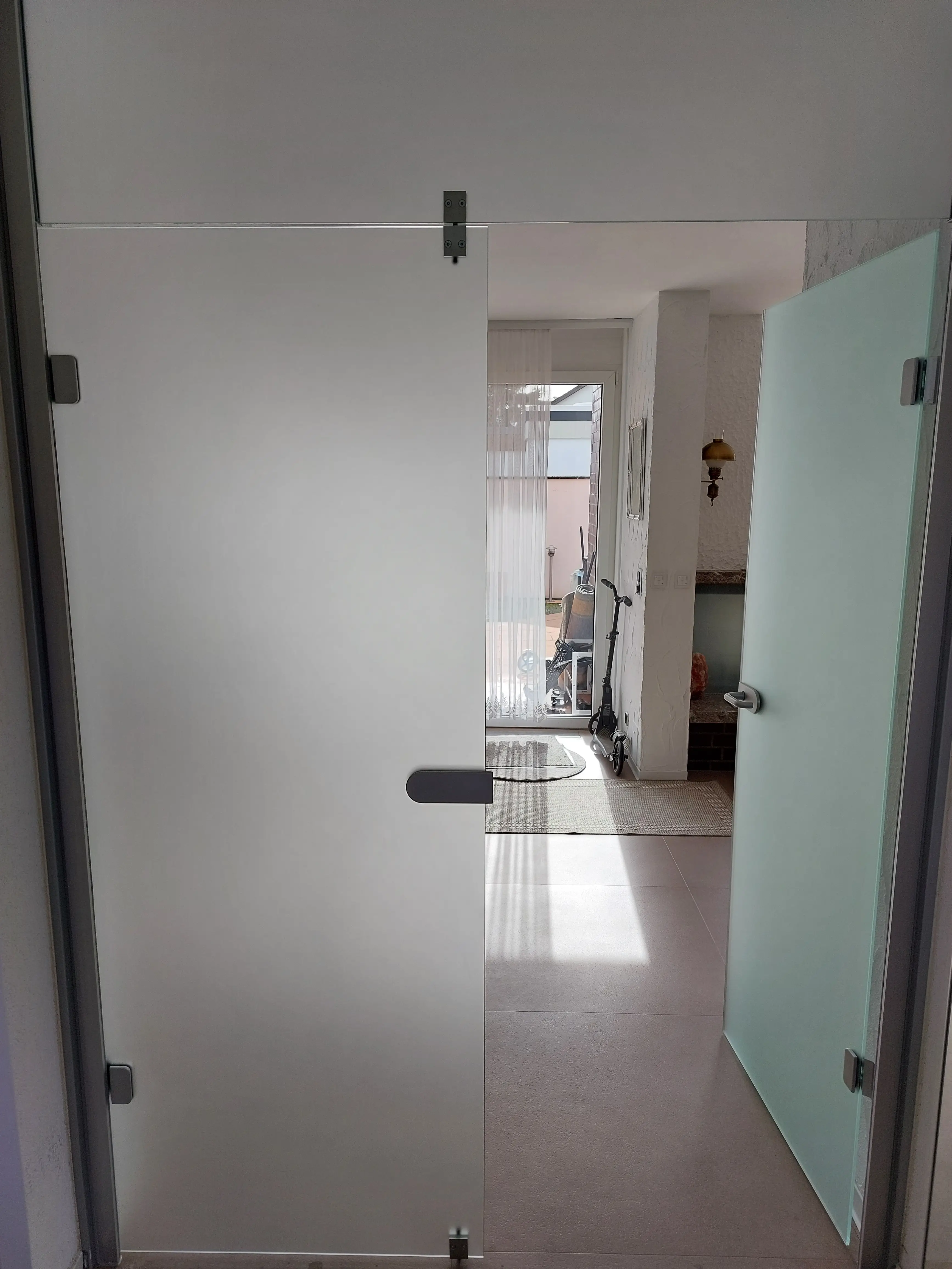 Moderne satinierte Ganzglas-Türanlage mit Aluminiumrahmen und geöffnetem Glasseitenteil im Eingangsbereich eines Wohnhauses.