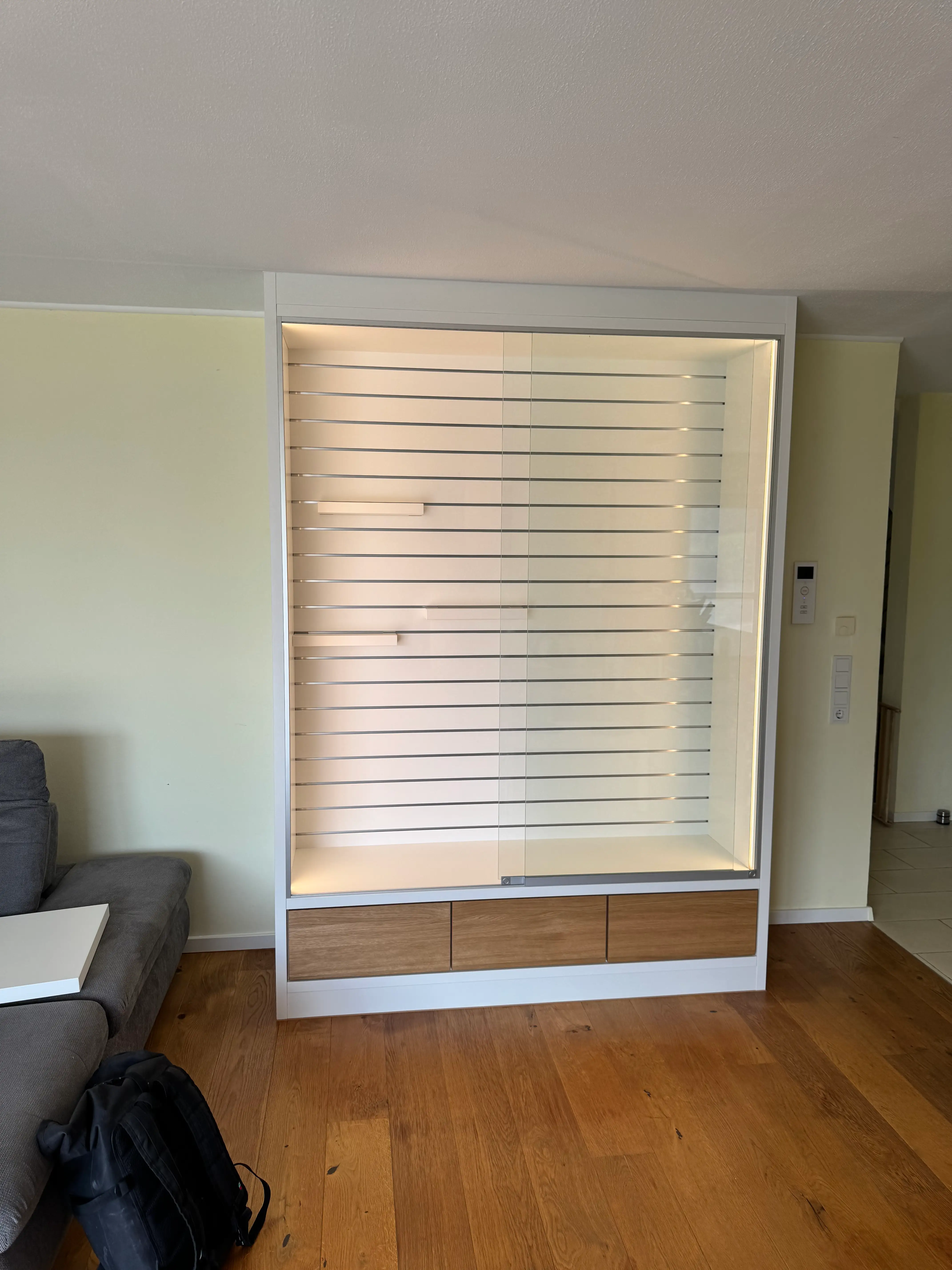 Individuelle Präsentationswand mit beleuchteter Glasvitrine, verstellbaren Präsentationsböden und Schubladenfronten in geölter Eiche in Lampertheim.