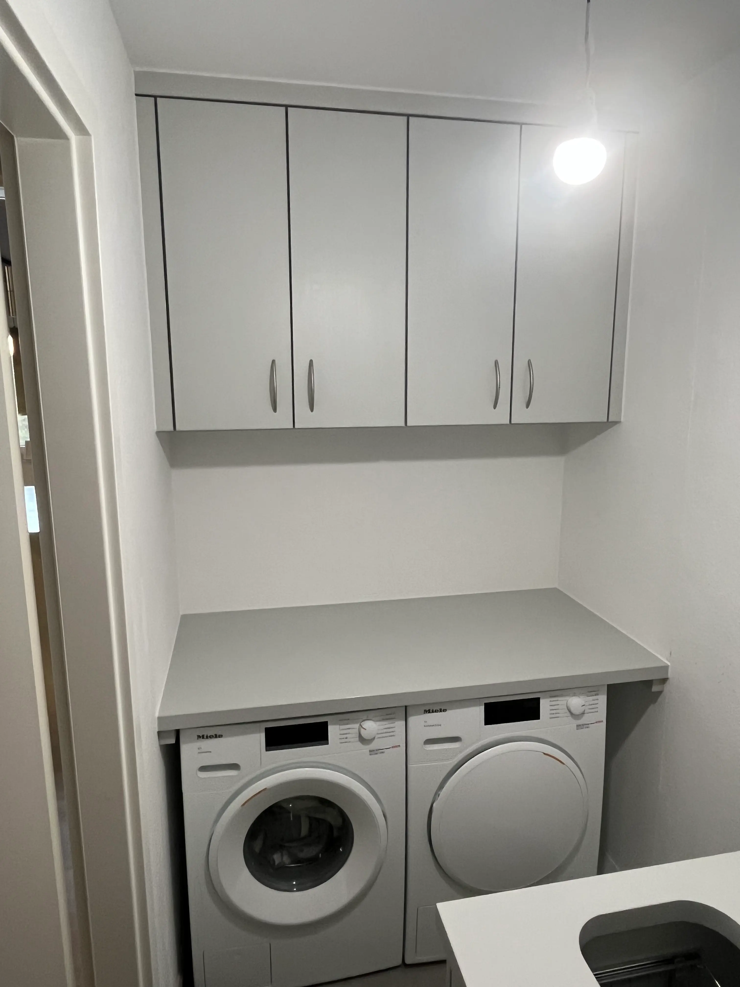 Maßgefertigter Hauswirtschaftsraum mit Arbeitsplatte über Waschmaschine und Trockner sowie individuell angepassten Hängeschränken in Plankstadt.