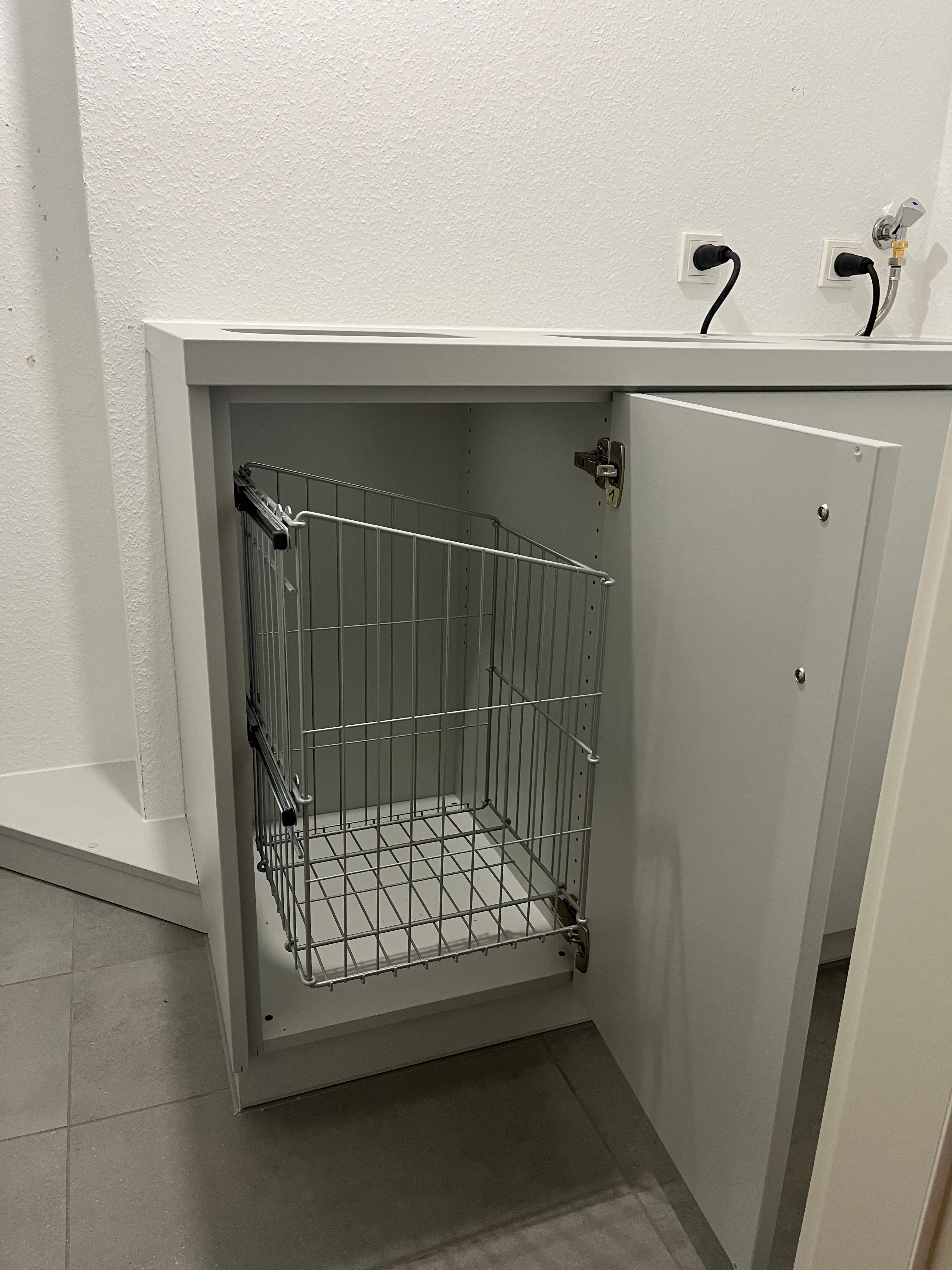 Ausziehbarer Wäschekorb in einem maßgefertigten Unterschrank sorgt für eine komfortable und platzsparende Wäscheaufbewahrung.