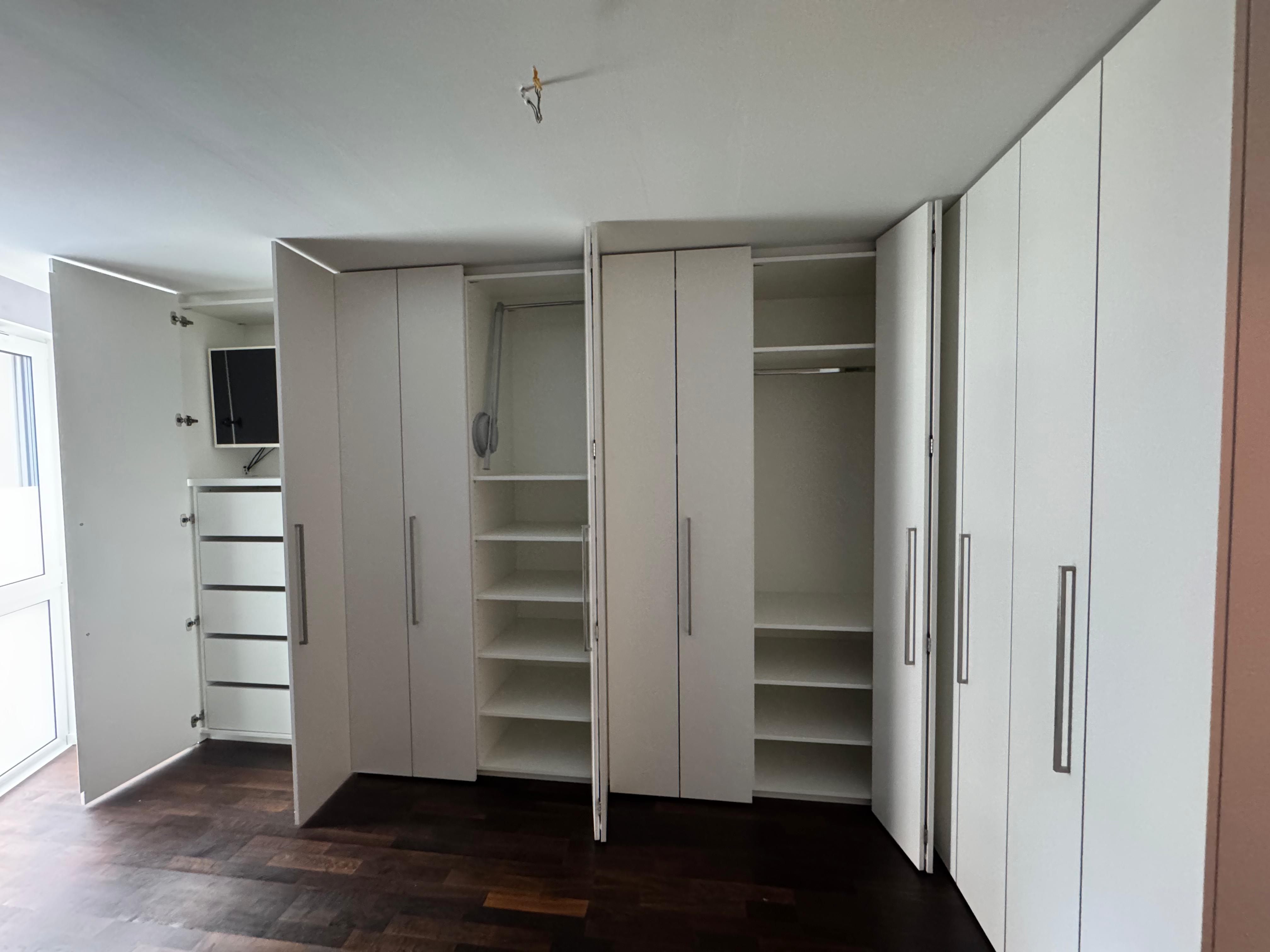 Geöffneter maßgefertigter Einbauschrank mit Kleiderlift, verstellbaren Fachböden und integriertem Homeoffice in einem Schlafzimmer in Weinheim.