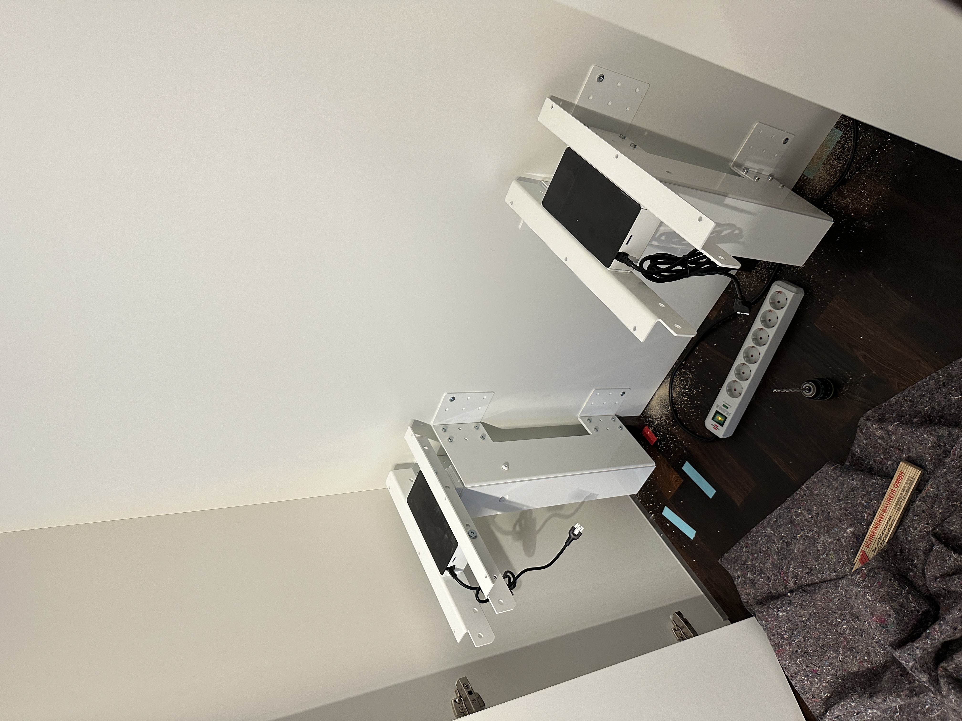 Vorbereitung eines elektrisch höhenverstellbaren Schreibtischs im integrierten Homeoffice einer maßgefertigten Einbauschrankanlage. Die Antriebseinheiten und Elektroanschlüsse sind vor der Montage der Arbeitsplatte im Schrank installiert.