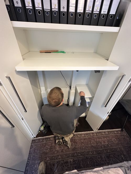 Montage des integrierten Homeoffice-Bereichs mit elektrisch höhenverstellbarer Arbeitsplatte in einer maßgefertigten Einbauschrankanlage. Die Technik und Kabelführung werden während der Endmontage im Schrank integriert.