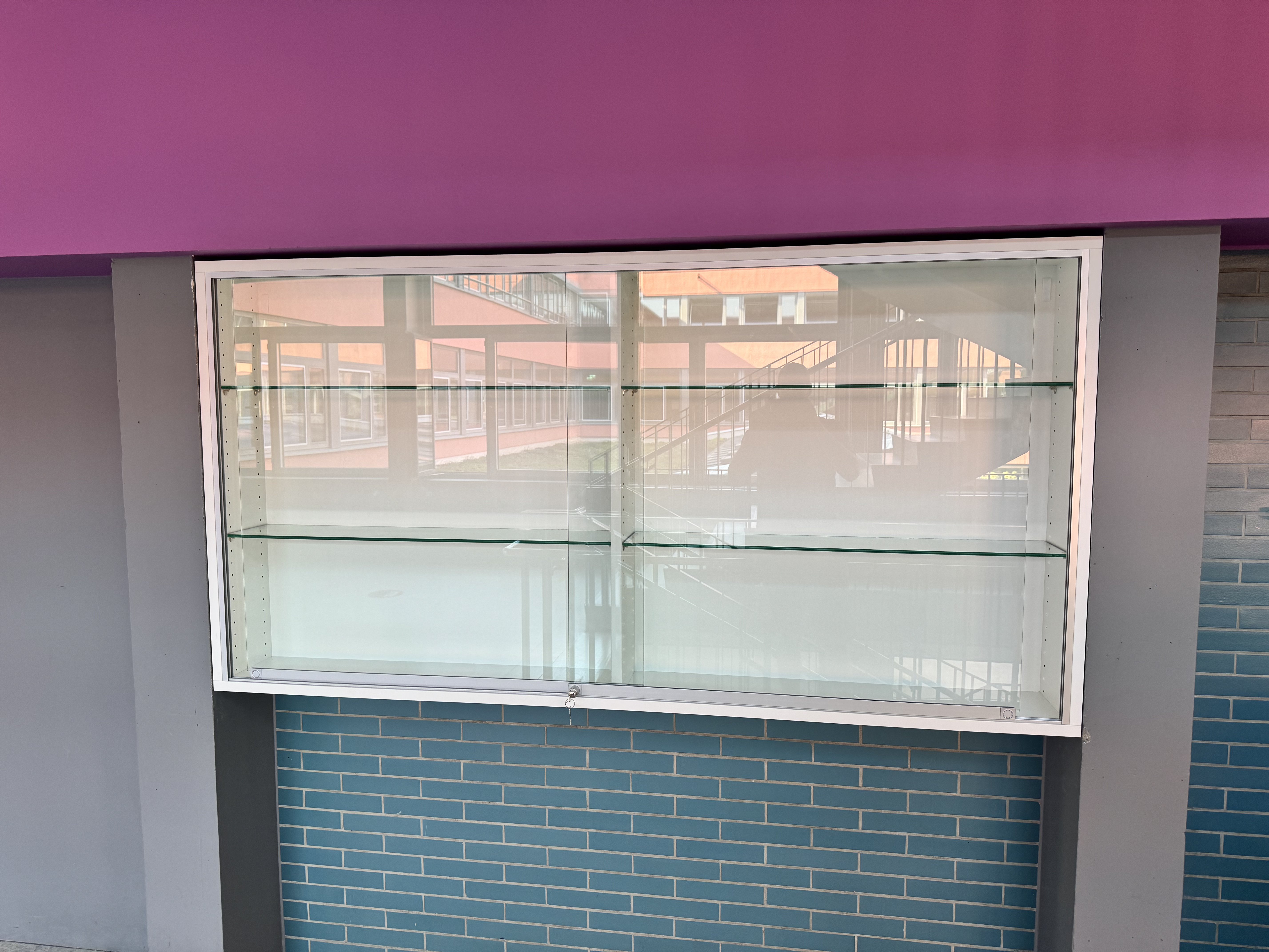 Maßgefertigte Glasvitrine mit abschließbaren ESG-Glasschiebetüren in einer Schule in Viernheim