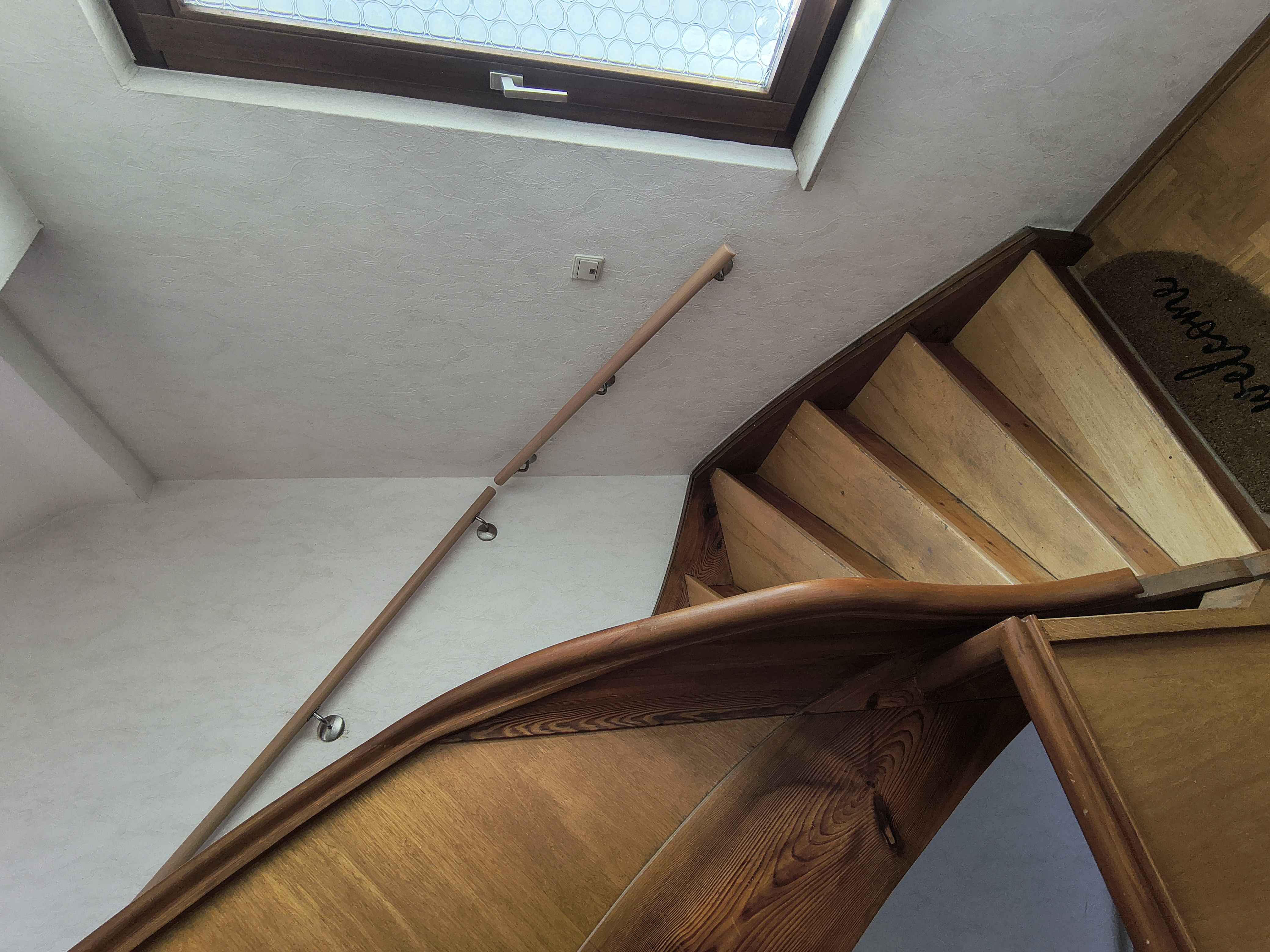 Maßgefertigter Buchenhandlauf mit Edelstahl-Wandhaltern an einer bestehenden Holztreppe im Eingangsbereich eines Wohnhauses in Viernheim.