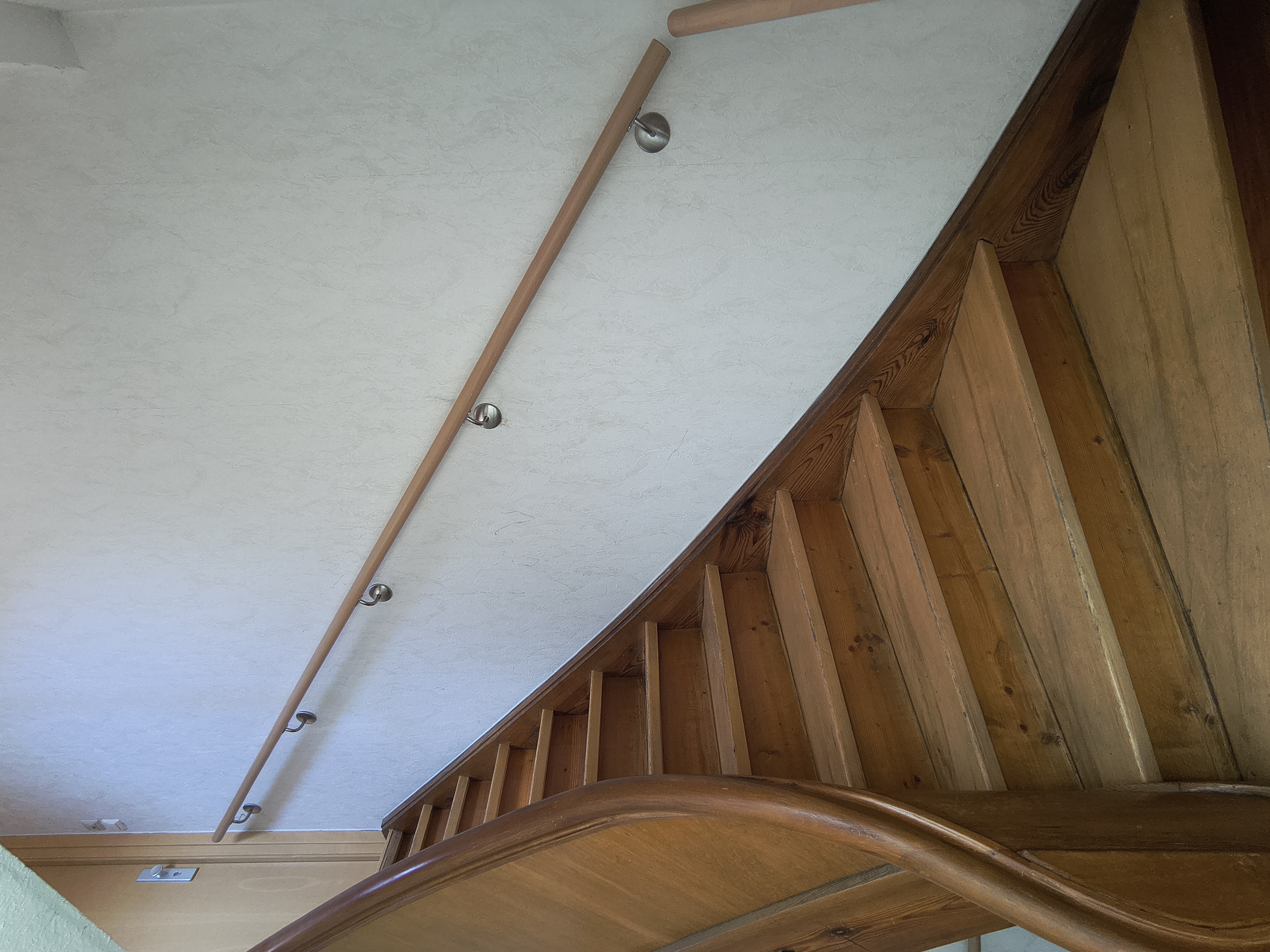 Passgenau gefertigter Handlauf aus Buche mit Edelstahl-Wandhaltern entlang einer bestehenden Holztreppe in einem Wohnhaus in Viernheim.
