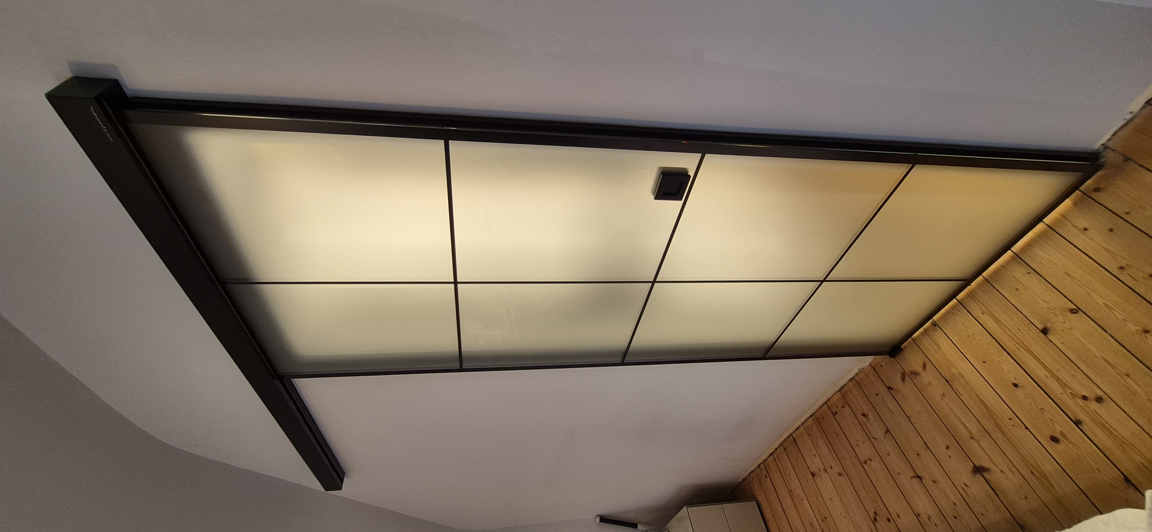 Loft-Schiebetür aus satiniertem 8 mm ESG-Glas mit schwarzem Sprossendesign und schwarzen Beschlägen als Zugang zur Ankleide in einem Schlafzimmer in Viernheim.