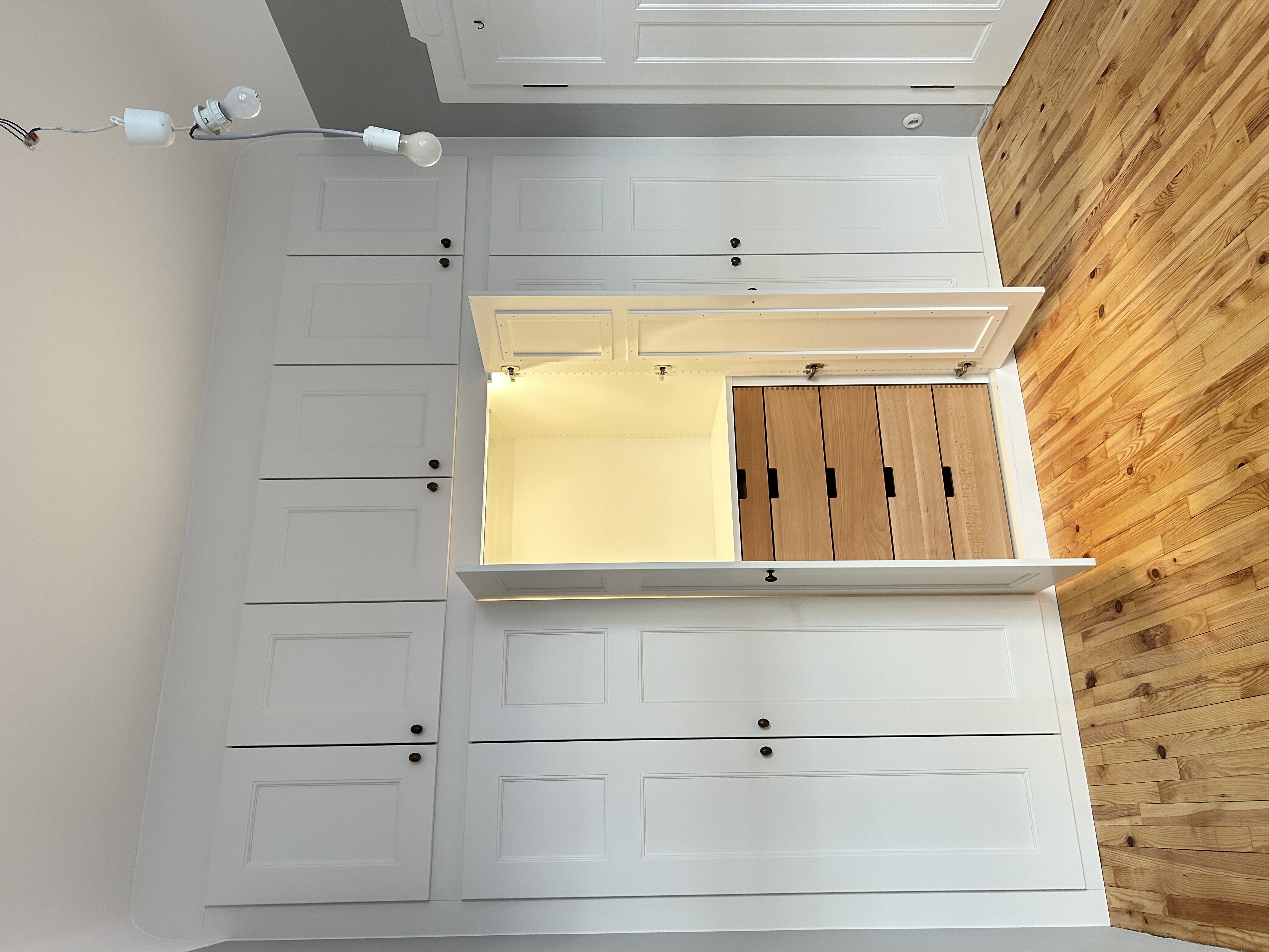 Maßgefertigter weißer Einbauschrank in Mannheim mit geöffneten Rahmentüren, integrierter LED-Beleuchtung und fünf Schubkästen aus Buche.