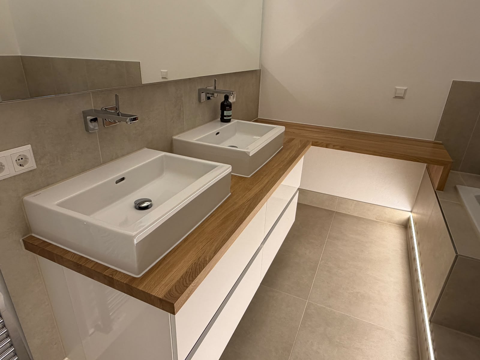 Maßgefertigte Waschtischplatte aus Eiche-Leimholz über Eck mit zwei Aufsatzwaschbecken und weißen Badmöbeln in Brühl.