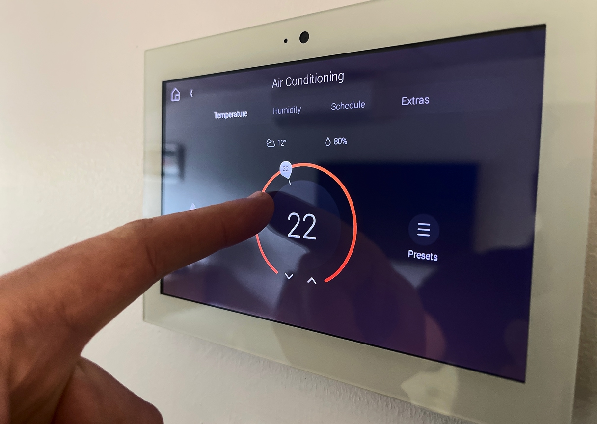 Person using a wall-mounted smart climate panel to adjust room temperature.