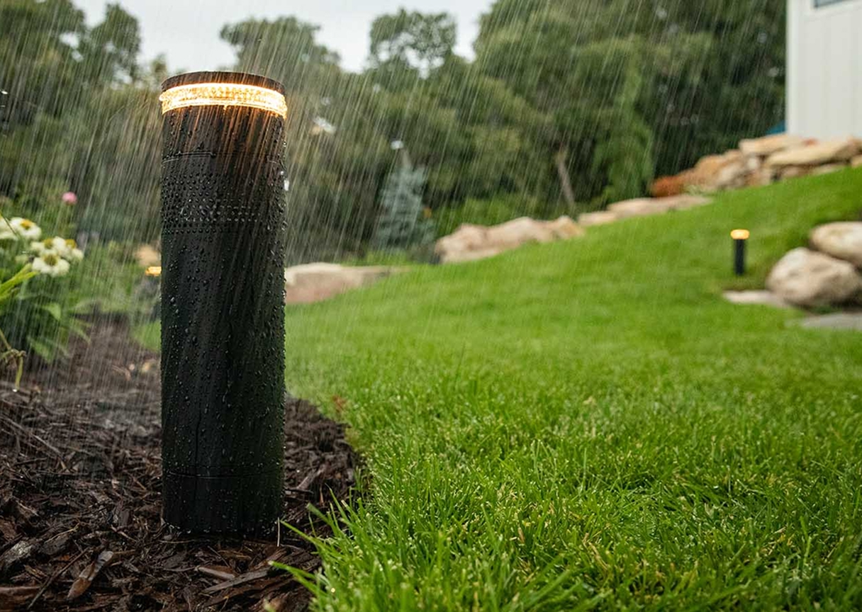 Weatherproof garden light fixture in landscaped backyard, part of automated outdoor lighting system.