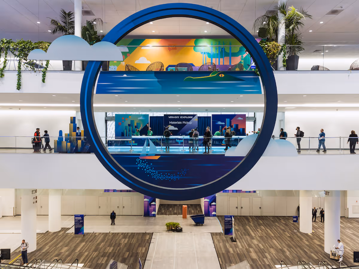 Large circular wall decoration with a sailboat and alligator design, hanging in a multi-level convention center with people walking nearby.