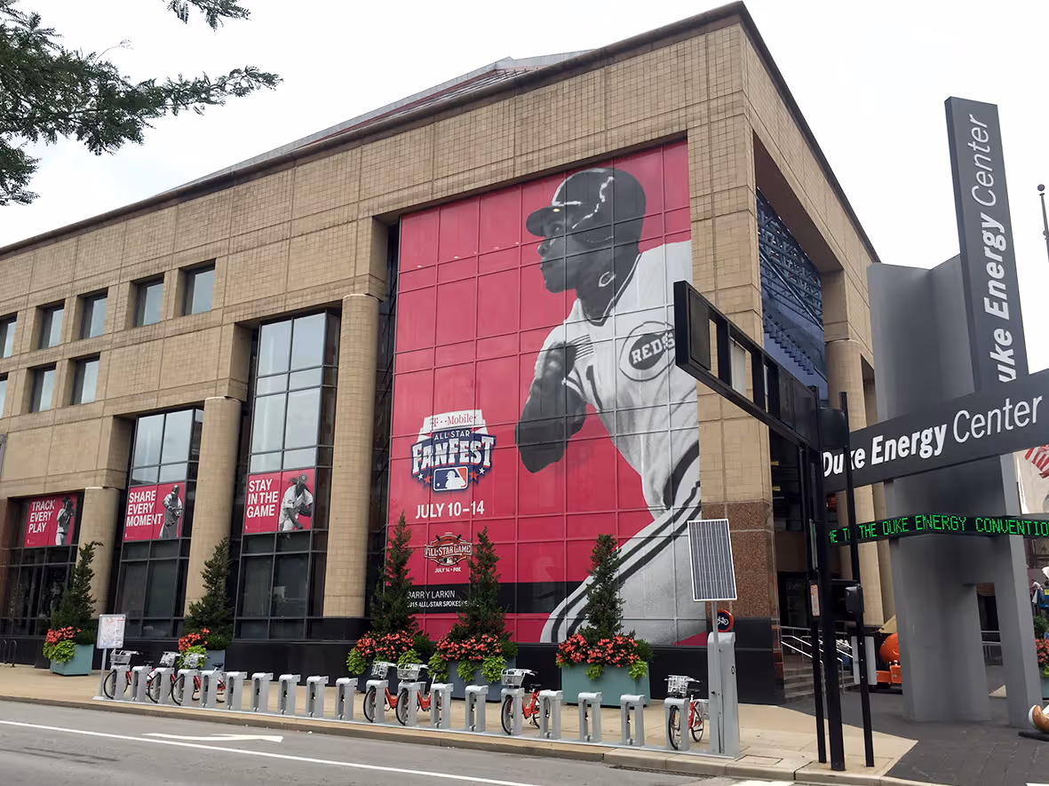 Large mural of a Cincinnati Reds baseball player on the corner of a building with banners promoting T-Mobile All-Star FanFest July 10-14 at the Duke Energy Center.