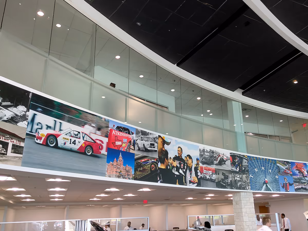 Curved wall inside a showroom displaying a large collage of racing car photos, team members, and historic scenes.