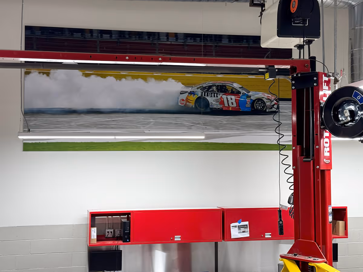 A silicone edged graphic frame with a Race car number 18 drifting on a track with smoke trailing behind it, displayed on a garage wall.