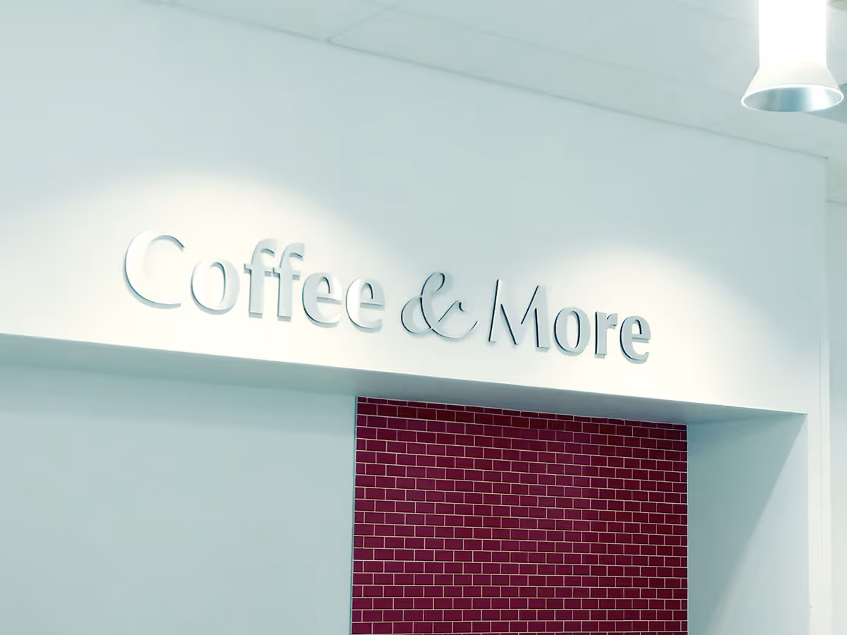 Indoor sign with the words 'Coffee & More' that has been custom fabricated on a white wall above a red brick accent wall.