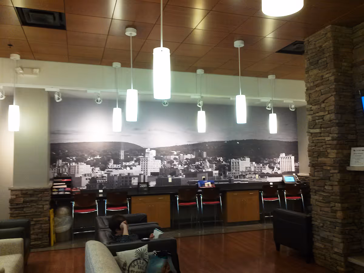 Modern lounge area with black and white cityscape mural, pendant lights, chairs, and a person reading.