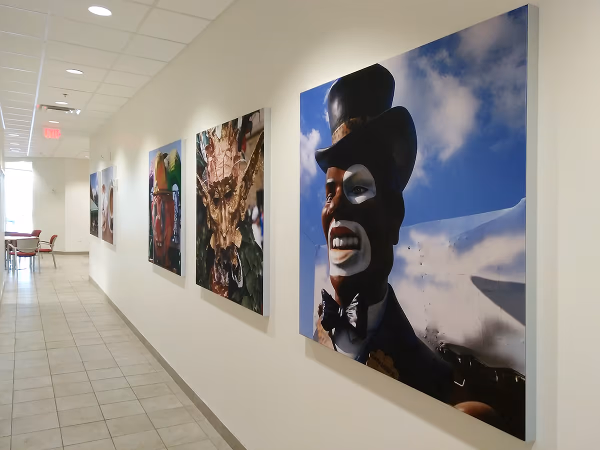 Hallway with tiled floor and walls displaying silicone edged graphic frame with colorful, large fabric prints of artistic masks and faces.