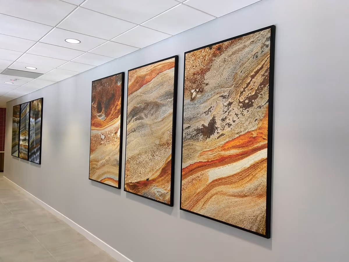 Modern hallway with gray walls and floor tiles featuring a series of Silicone edged graphic frames with abstract, earth-toned fabric prints. 