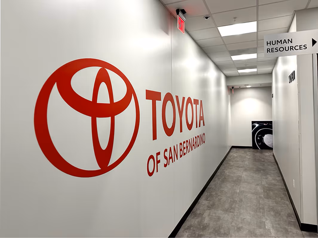 Hallway with a large red Toyota logo fabricated and installed saying 'Toyota of San Bernardino' on the left wall and a 'Human Resources' sign on the right.