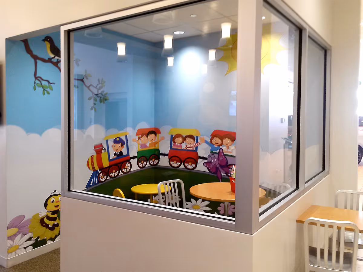 Children's playroom with colorful train mural showing kids waving, surrounded by cartoon flowers, a bee, and a bird on the wall.