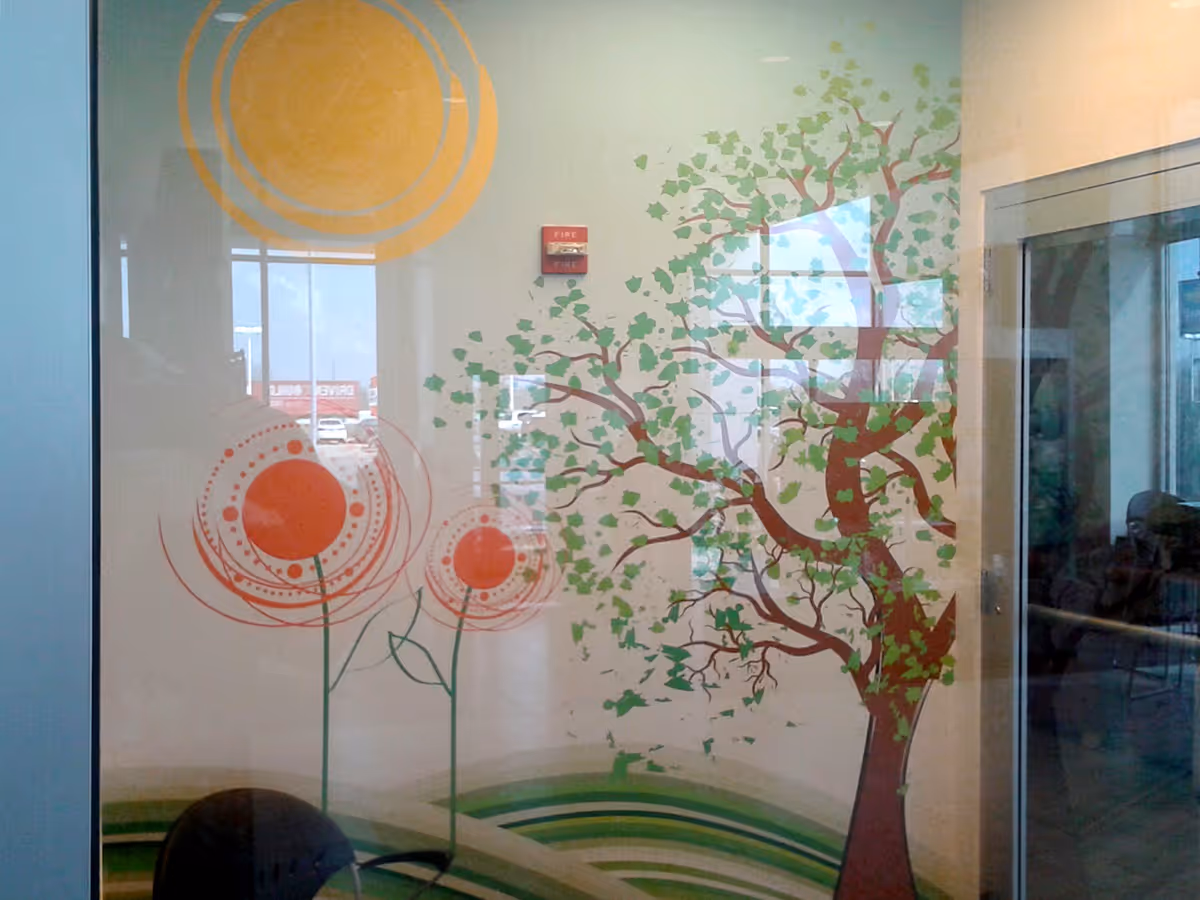 Wall mural in a room depicting a large tree with green leaves, two stylized orange flowers, and a yellow sun.