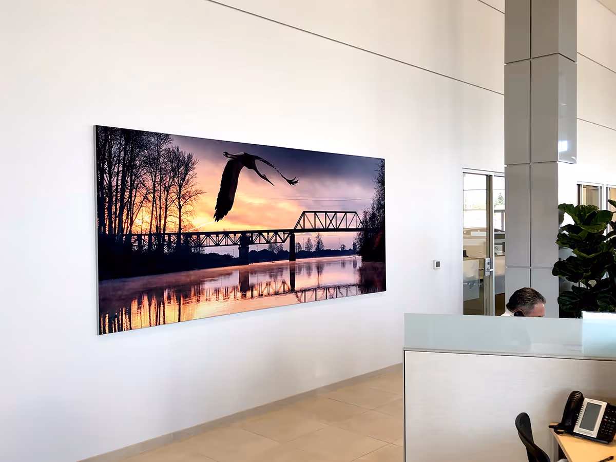 Modern office reception area with a large Silicone Edged Graphic Framed Fabric print  of a bird flying over a river at sunset by a bridge.
