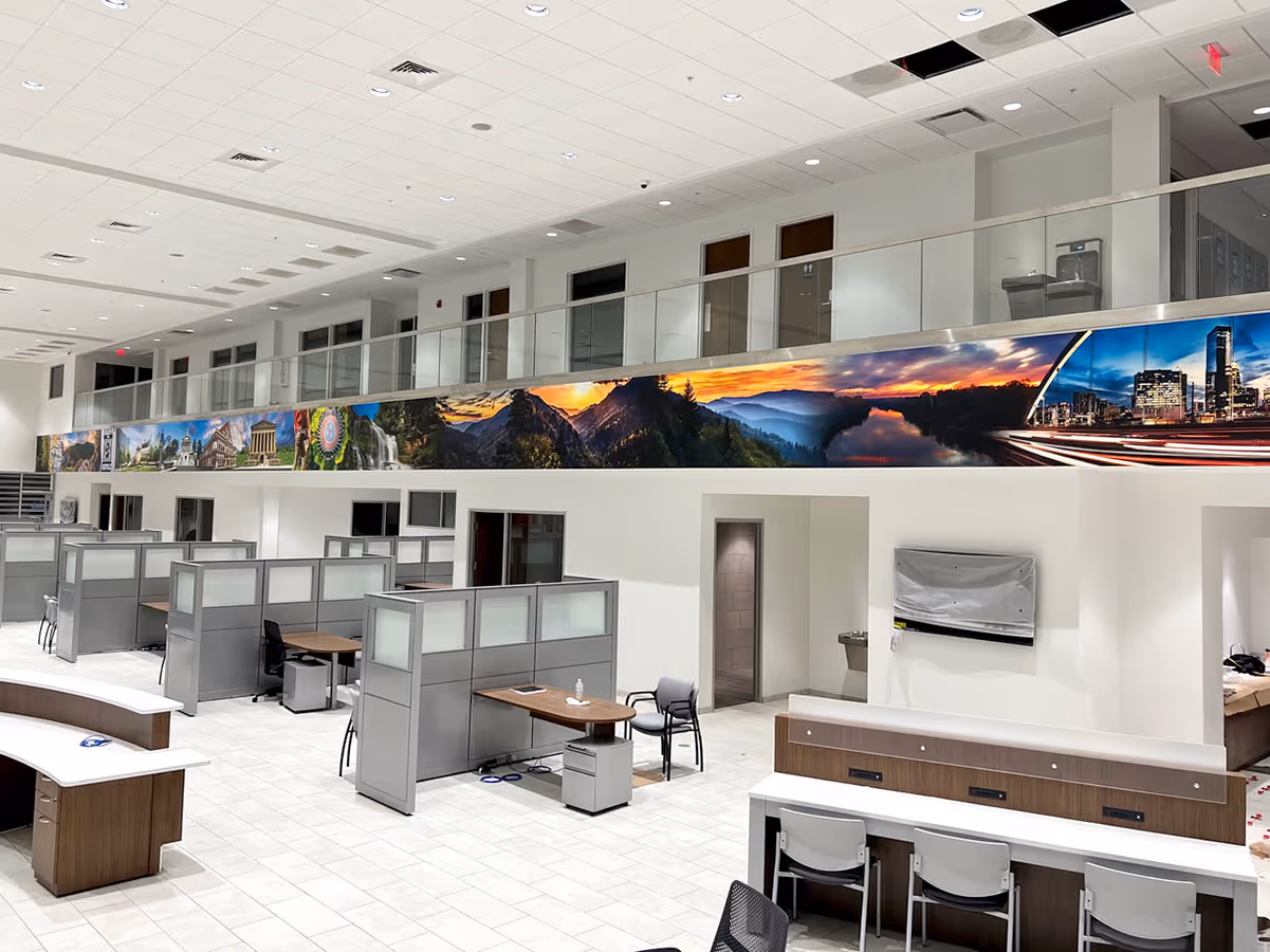 Modern open office space with cubicles, desks, chairs, and a panoramic mural of natural and urban landscapes along the upper wall.