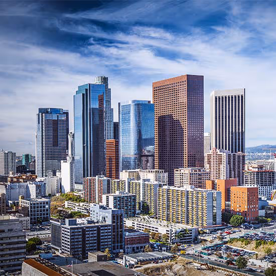 Downtown Los Angeles skyline with modern high-rise buildings under a partly cloudy blue sky.