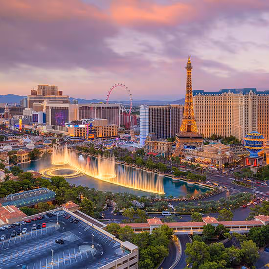 Las Vegas Strip at sunset with illuminated Bellagio fountain, replica Eiffel Tower, and High Roller Ferris wheel.