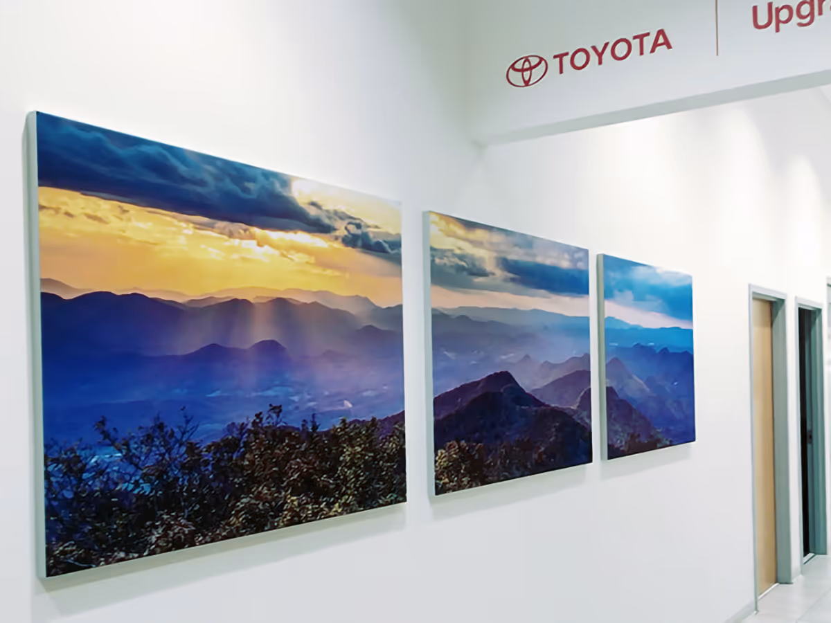 Three wall-mounted Silicone Edged Graphic frame with Fabric prints showing mountain ranges under a sunset sky, in a hallway with Toyota branding above.