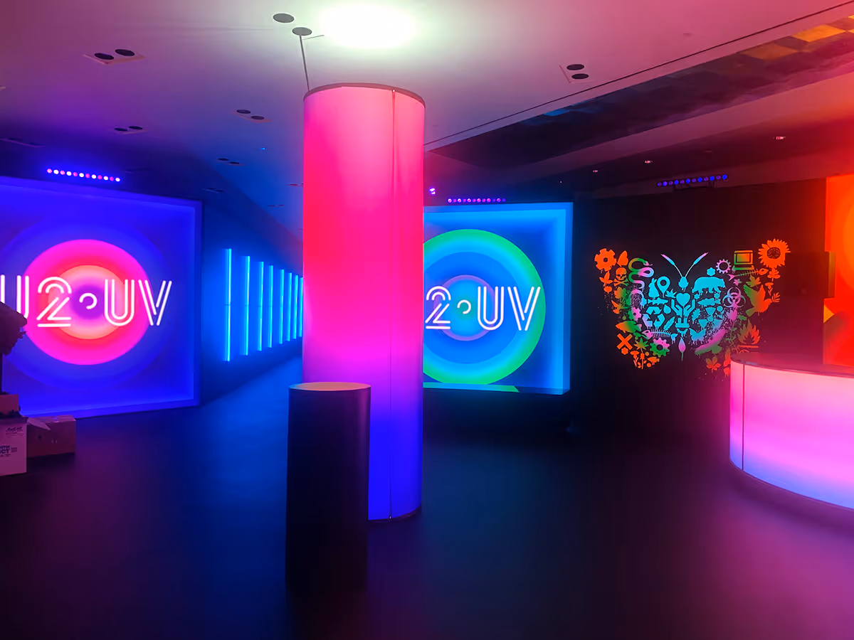Dark room with colorful neon lights including two circular signs reading 'u2oUV' and a bright pink illuminated pillar in the center.