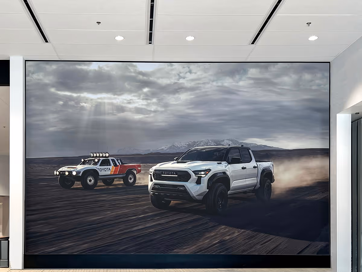 A large wall paper decal featuring two Toyota pickup trucks driving on a dusty terrain with mountains and a cloudy sky in the background.