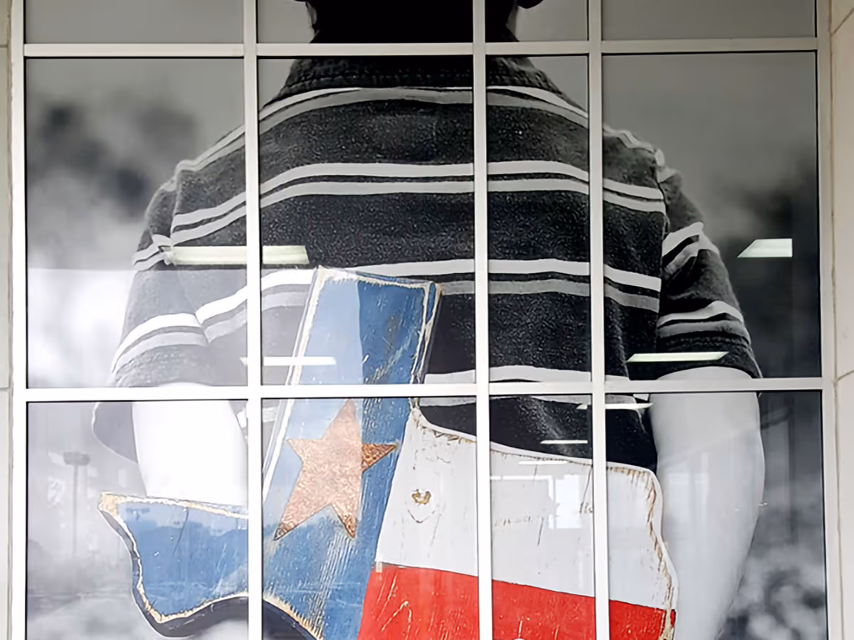 Window Decal showing a Back view of a person in a striped shirt holding wooden Texas state cutouts painted with the Texas flag colors.