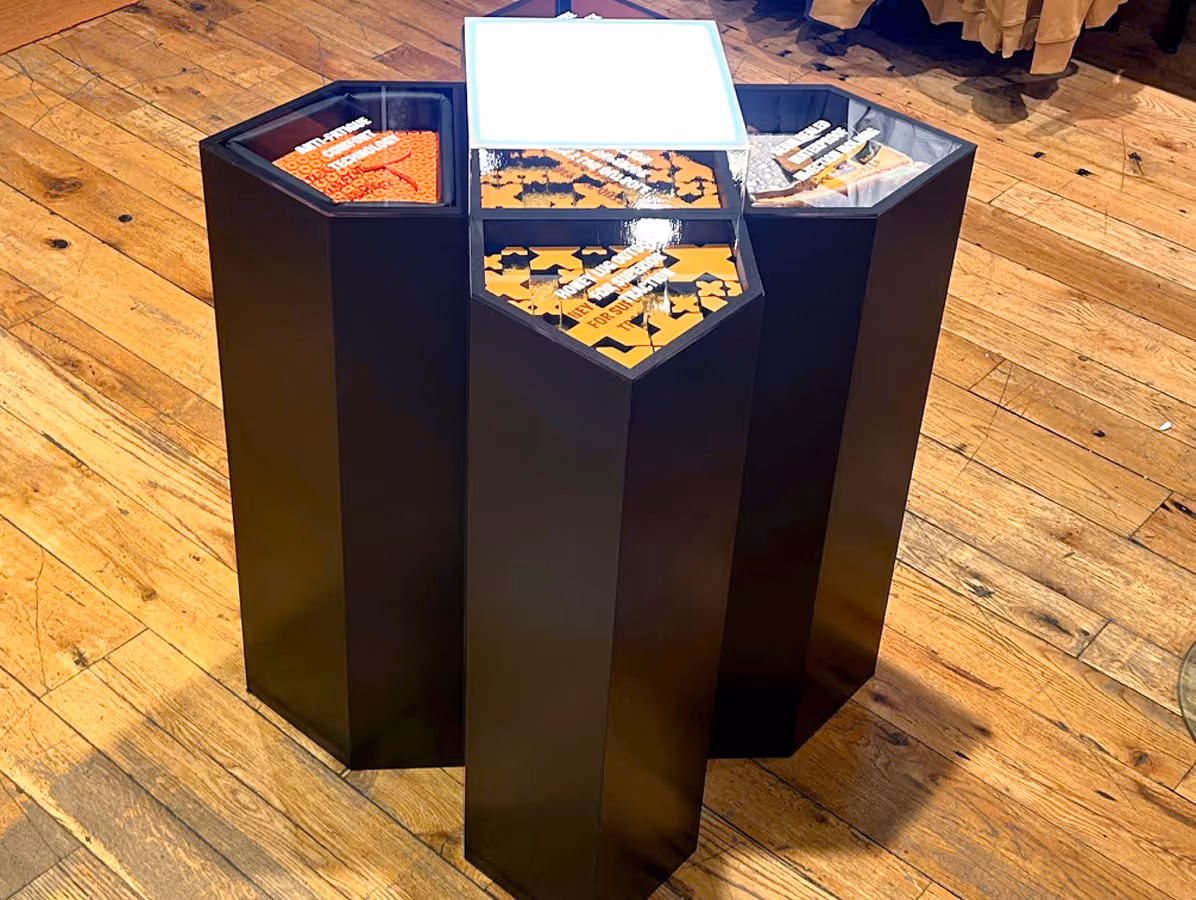 Hexagonal black pedestal with five compartments containing puzzle pieces and text labels on a wooden floor.