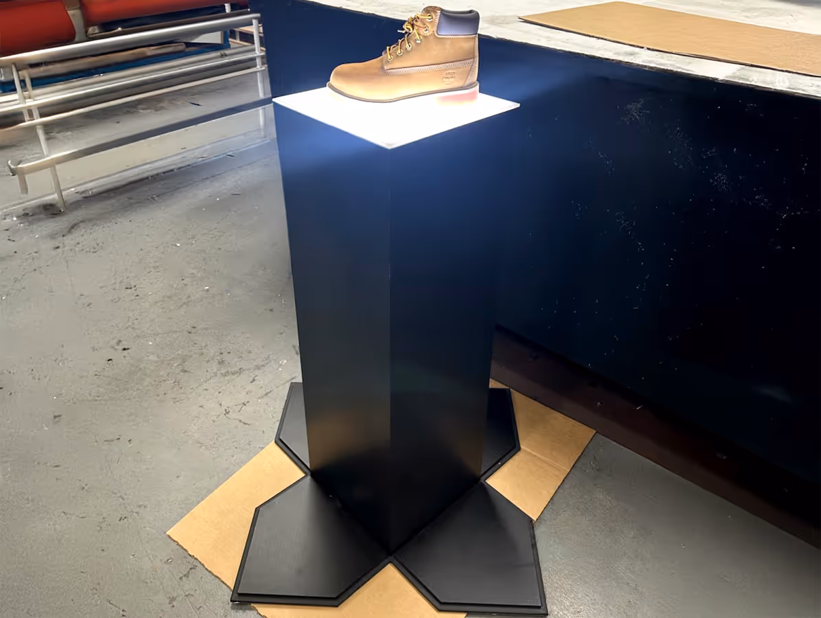 Leather work boot displayed on a black pedestal with a glowing white top in an industrial setting.