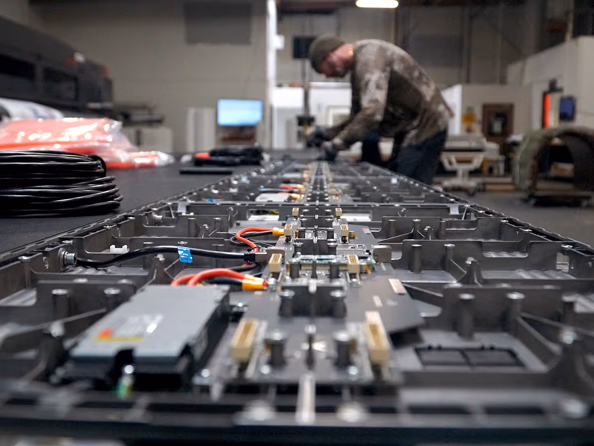 Worker assembling or inspecting electronic components on a long metal framework in an industrial setting.
