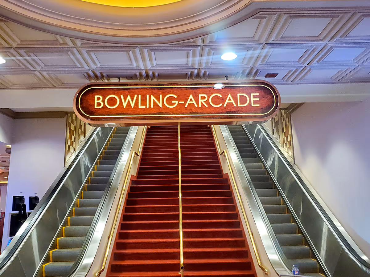 Red-carpeted stairs flanked by two escalators under a customized fabricated sign reading 'BOWLING-ARCADE'.
