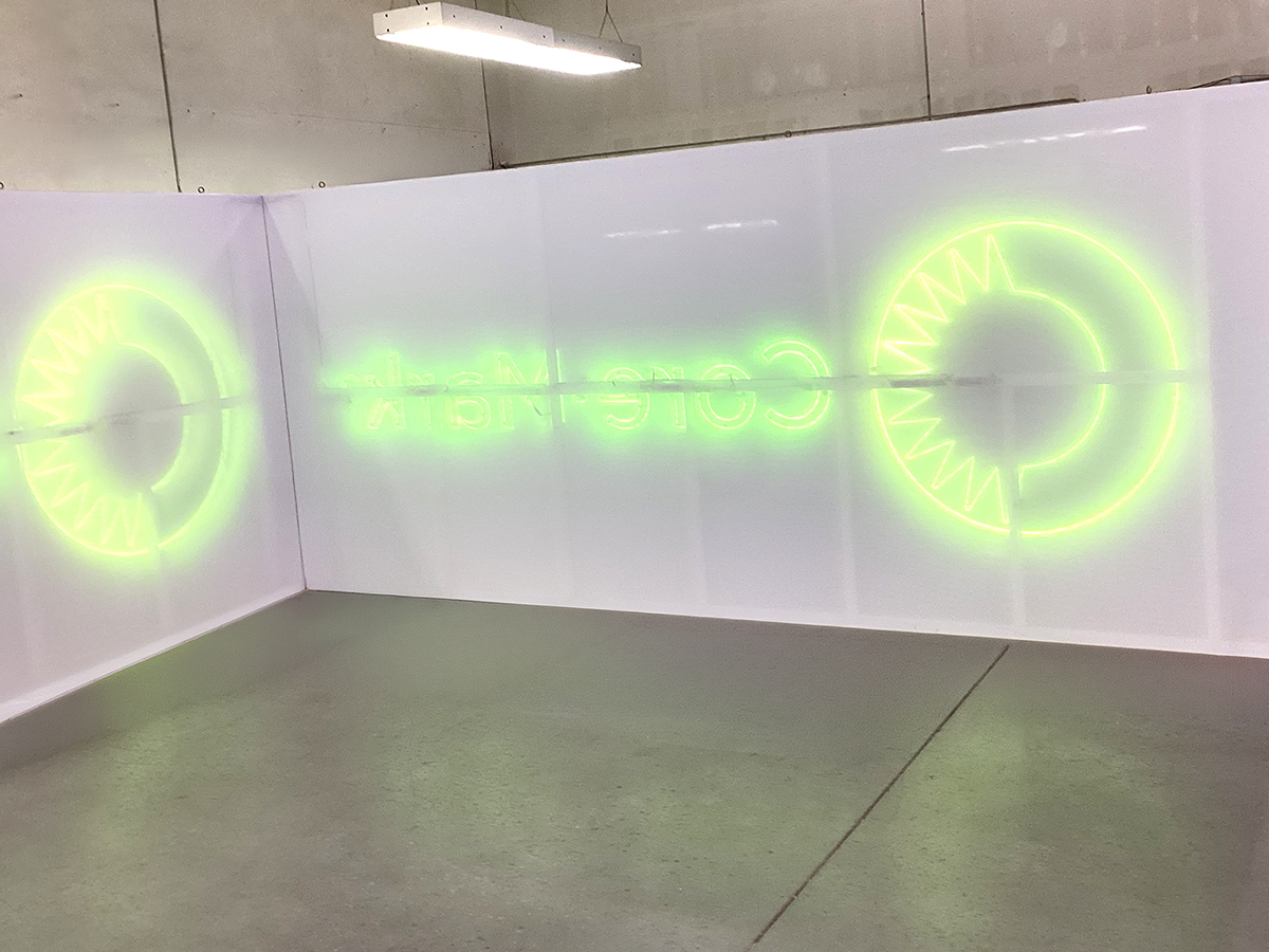 Neon green circular designs and reversed text glowing on white panels in an industrial space.