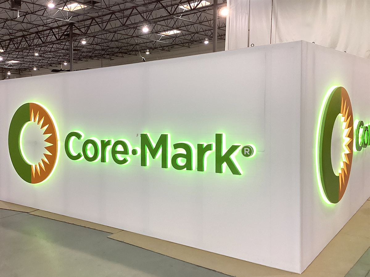 Illuminated Core-Mark logo with green and orange colors on a white corner wall in an industrial setting.