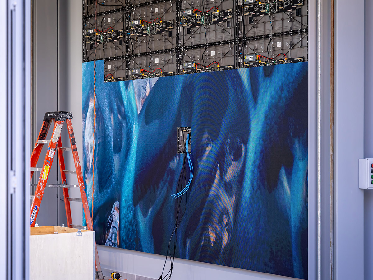 Large LED video wall in installation with visible electronic panels, cables, a red ladder, and construction equipment in a room.