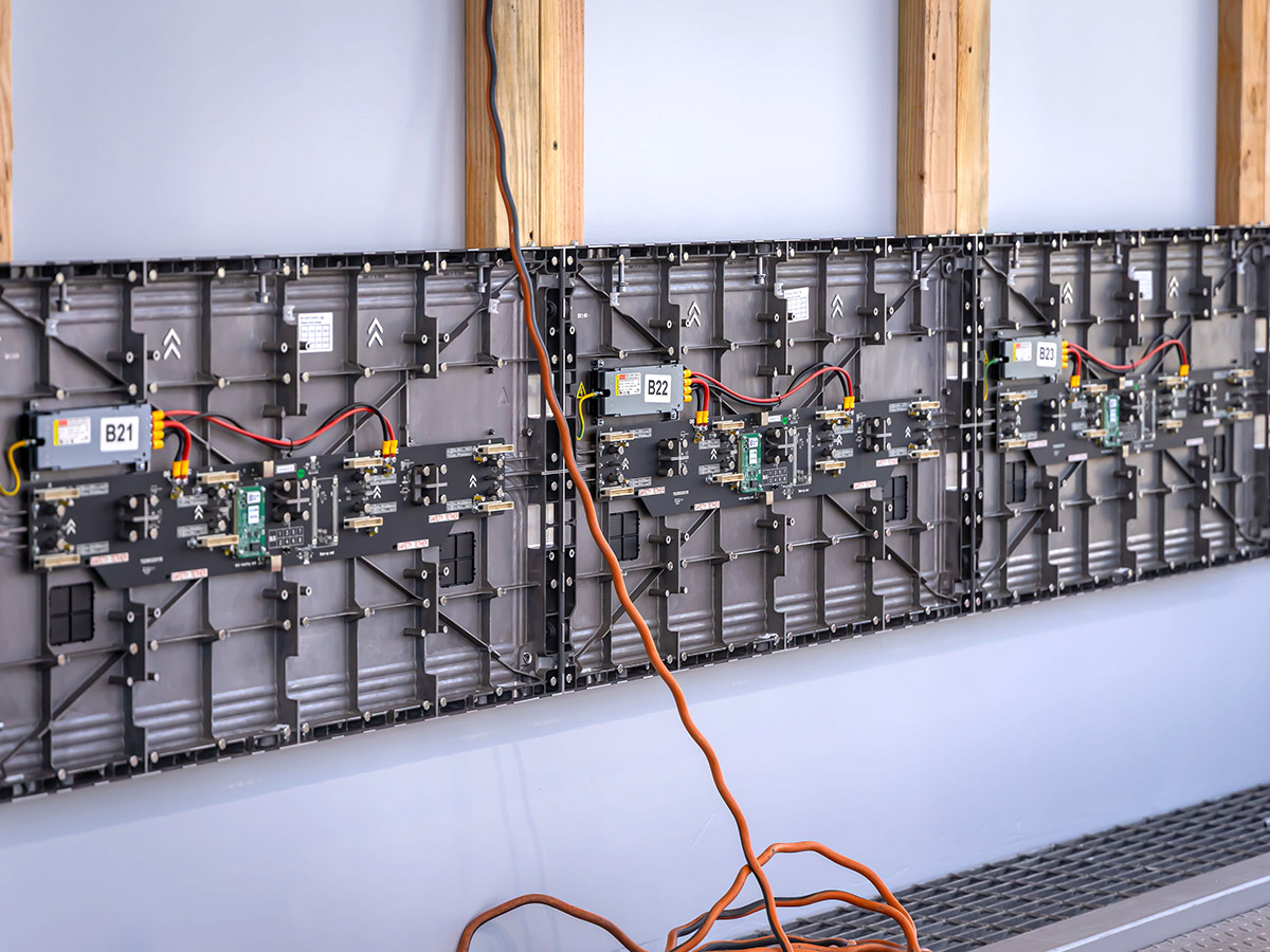 Back view of three connected LED display panels mounted on a wall with exposed circuit boards and cables.
