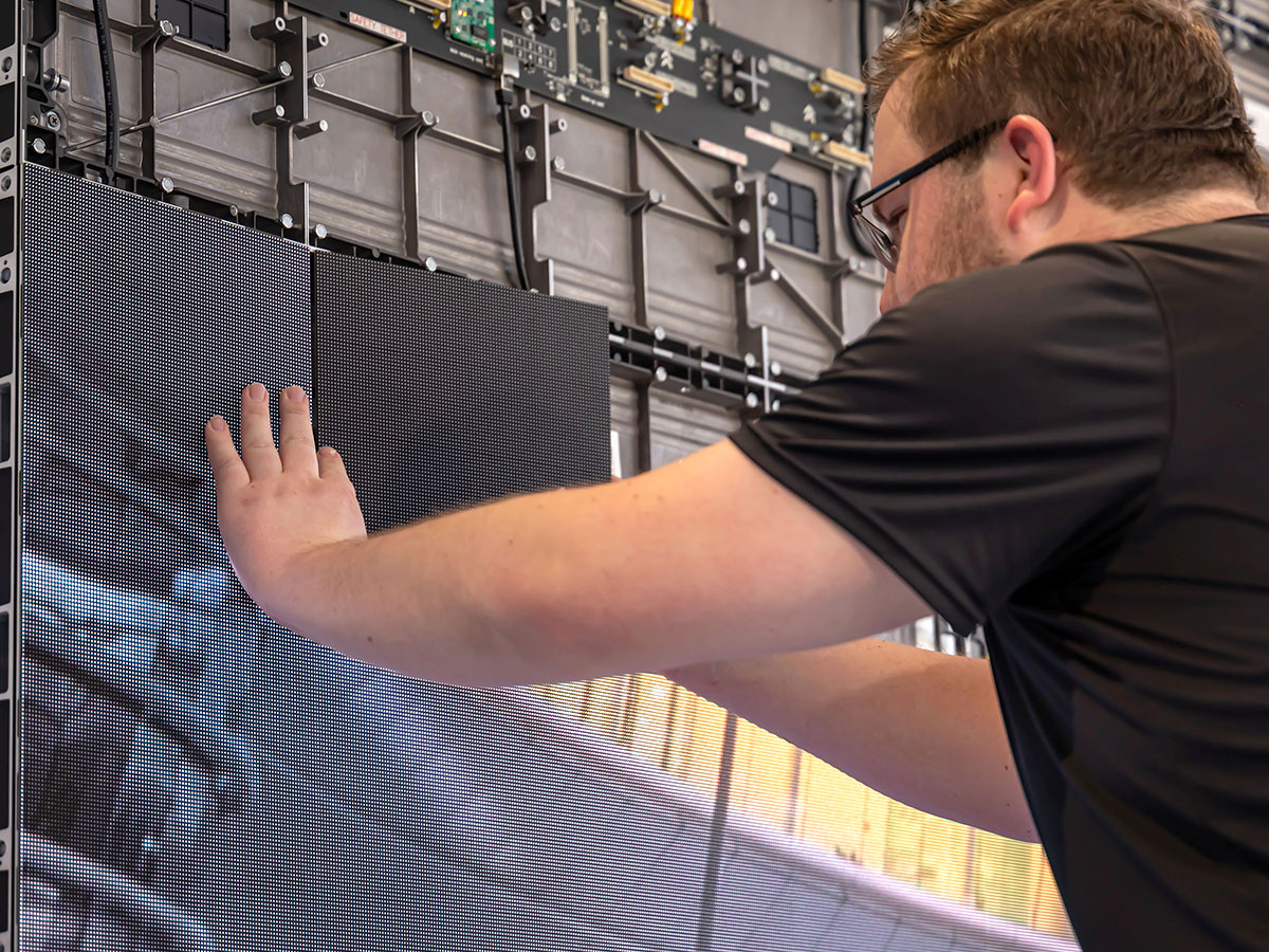 Technician with glasses installing or inspecting large LED display panels.